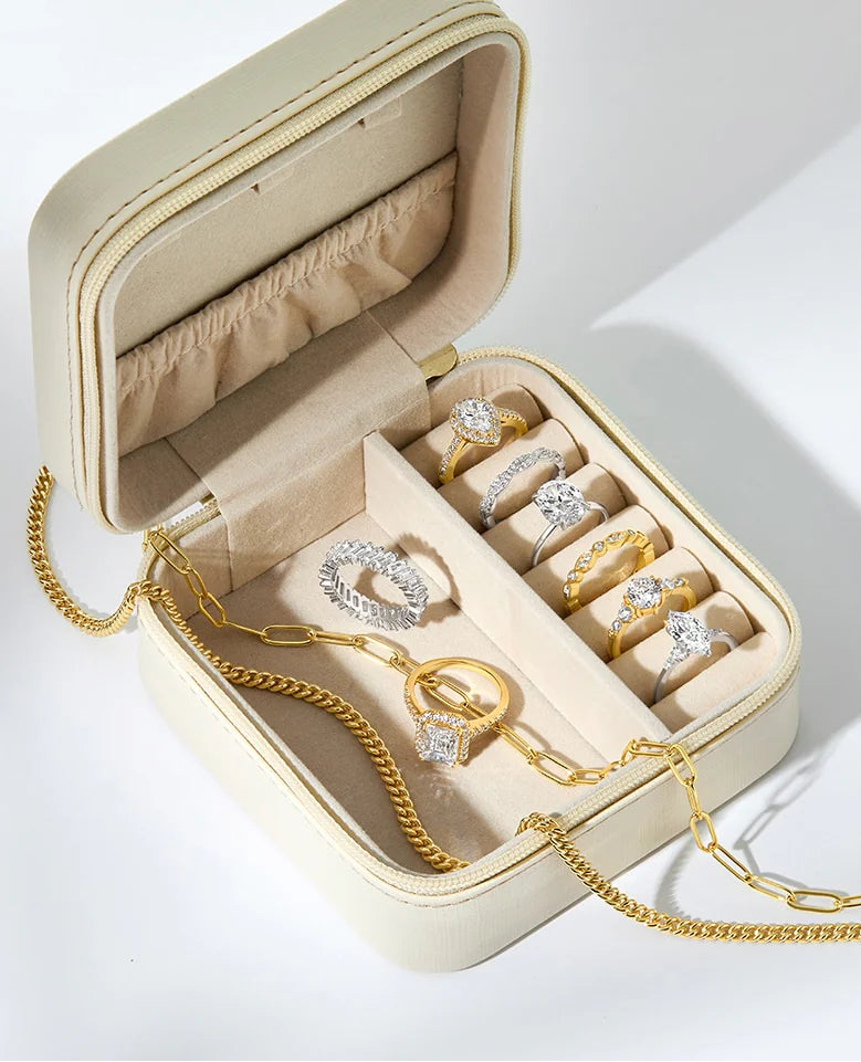 Open beige jewelry box with gold jewelry including rings and a necklace on a white background